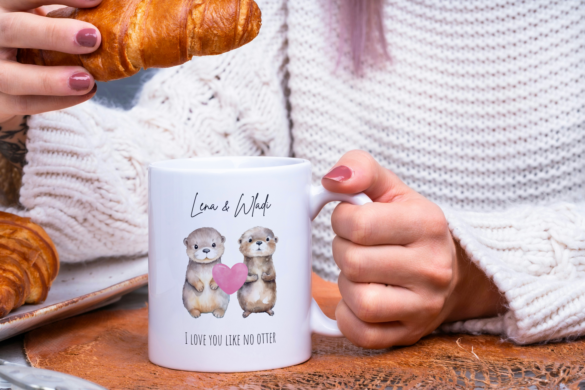 Eine Frau hält eine süße personalisierbare Otter Tasse in der Hand und isst ein Croissant