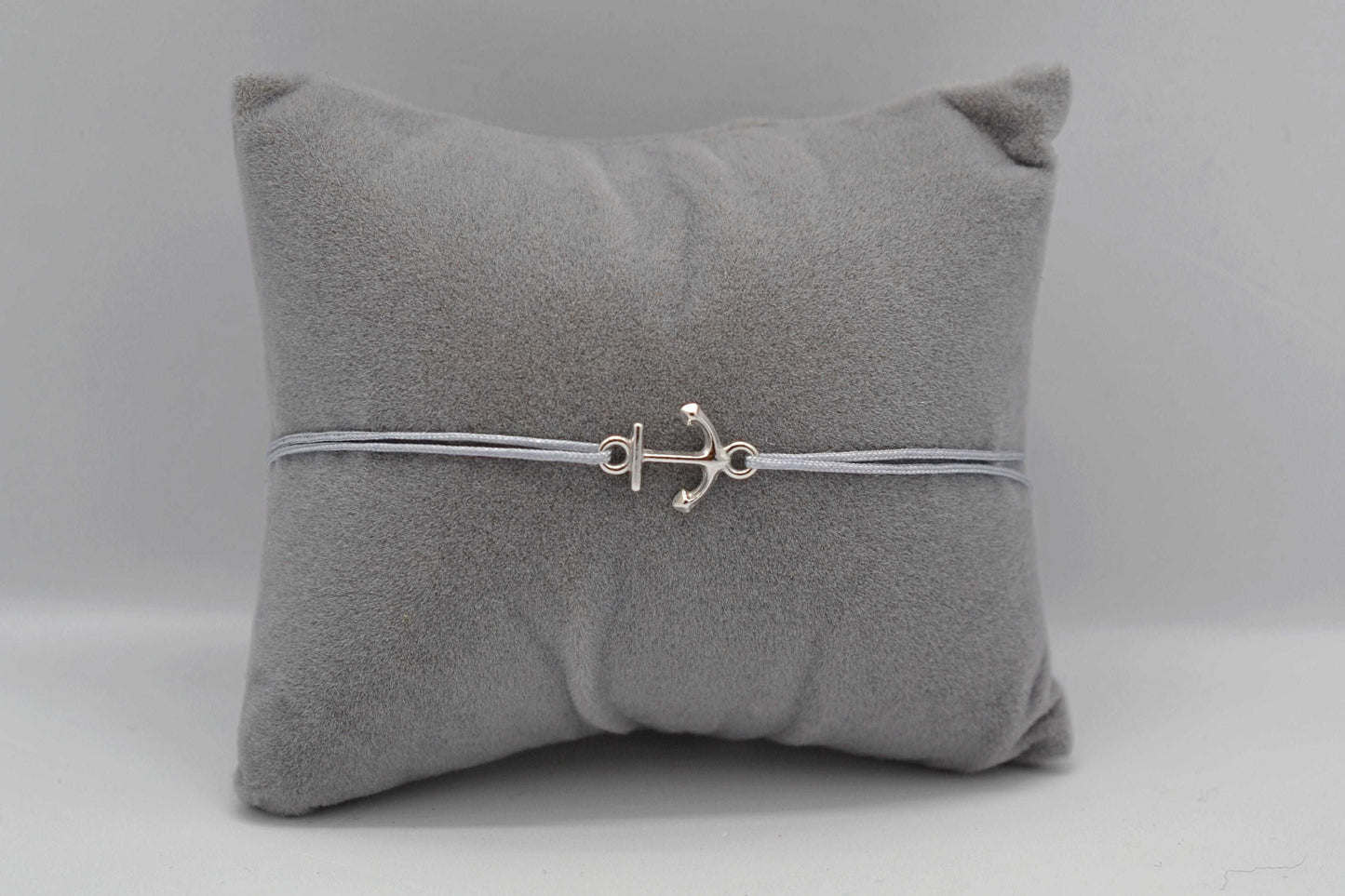 Silbernes Anker Armband mit grauem Bank auf einem grauen Schmuckkissen