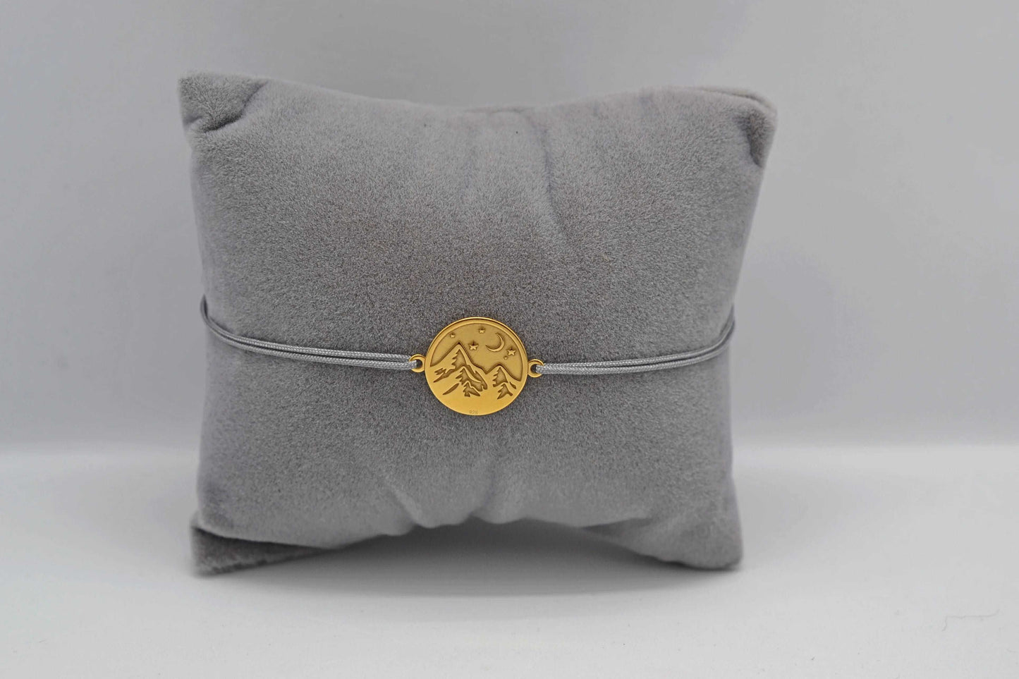 Goldenes Berg Armband mit grauem Band auf einem grauen Schmuckkissen