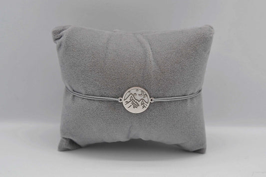 Silbernes Berg Armband mit grauem Band auf einem grauen Schmuckkissen