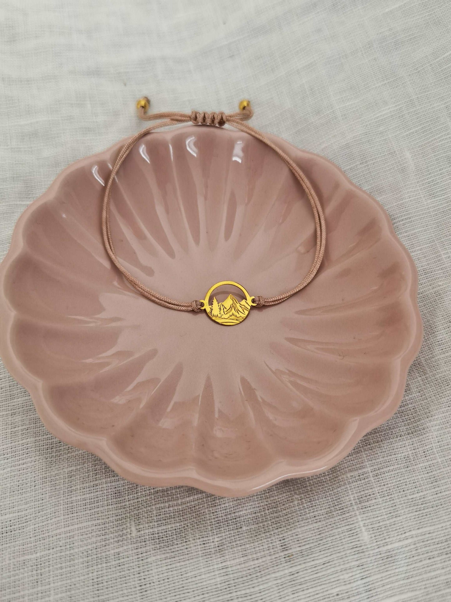 Ein goldenes Berg Armband mit beigem Band als Geschenk für Naturfreunde liegt in einer rosa Schmuckschale