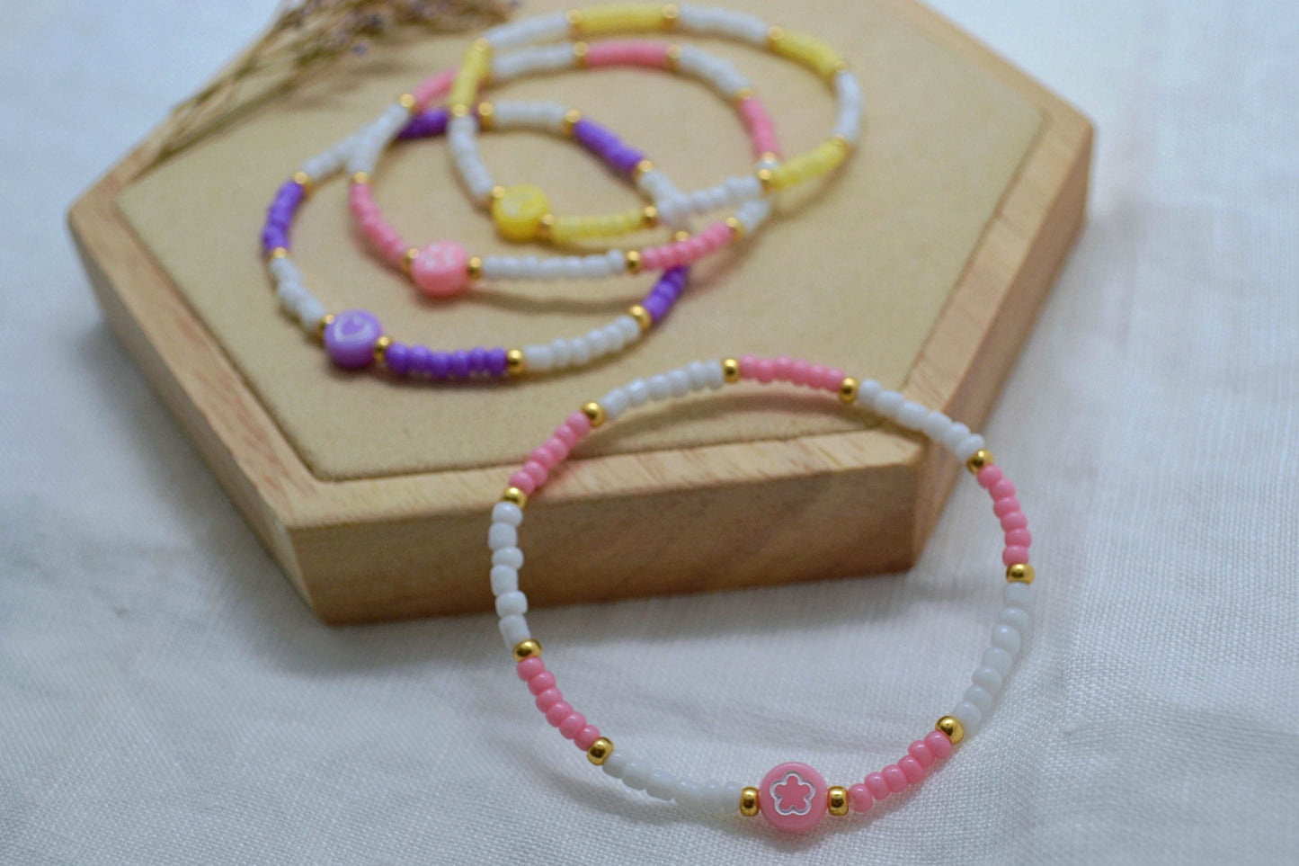 Nahaufnahme buntes Perlenarmband mit Blume, drei weitere Perlenarmbänder im Hintergrund