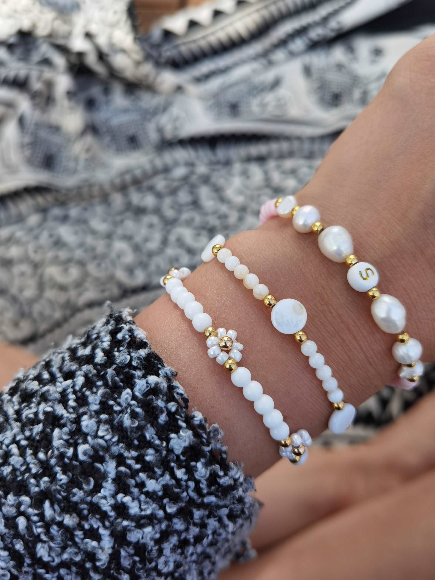 Tragefoto drei Armbänder. 1x Gänseblümchen Armband mit weißen Glasperlen, 1x Armband mit weißen Perlen und Perlmuttkreisen und ein personalisierbares Süßwasserperlen Armband mit dem Buchstaben "S"
