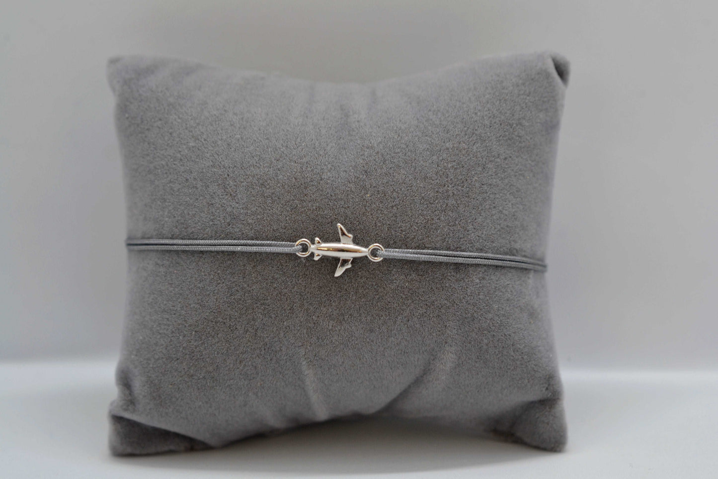 Silbernes Flugzeug Armband mit grauem Band auf einem grauen Schmuckkissen