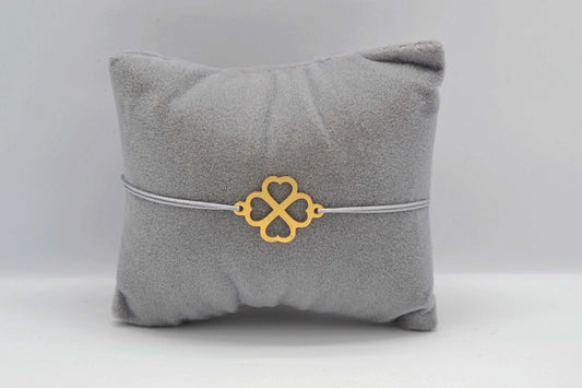 Filigranes Kleeblatt Armband in gold mit grauem Band auf einem grauem Schmuckkissen