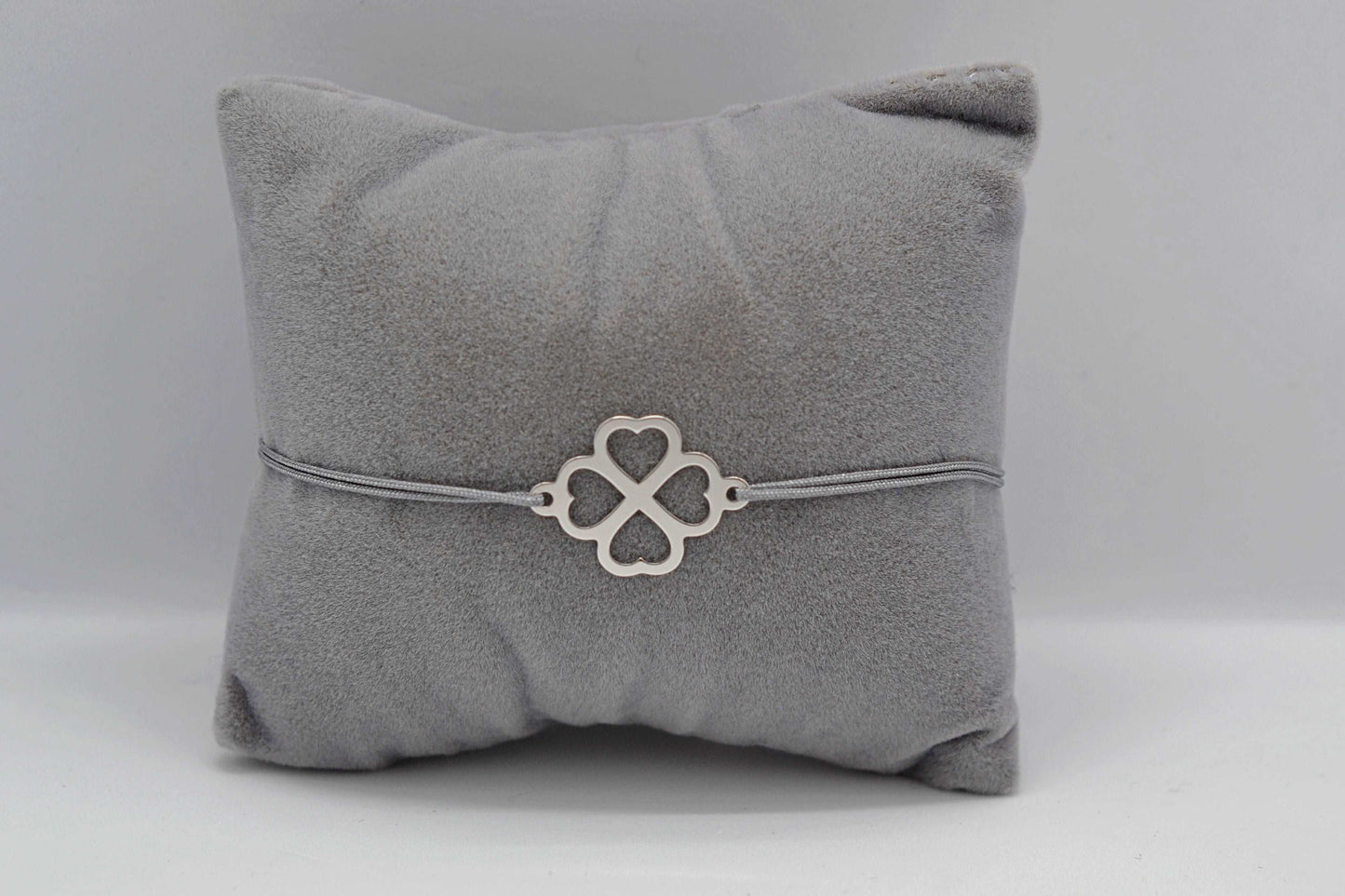 Kleeblatt Armband in silber mit grauem Band auf grauem Schmuckkissen