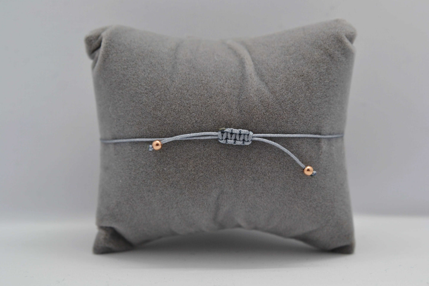Armband Makramee Verschluss graues Armband mit roségoldenen Perlen. Fotografiert auf einem grauen Schmuckkissen