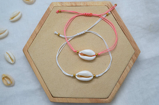Zwei Kauri Muschel Armbänder in rosa und weiß auf einem Holz Sechseck vor weißem Hintergrund