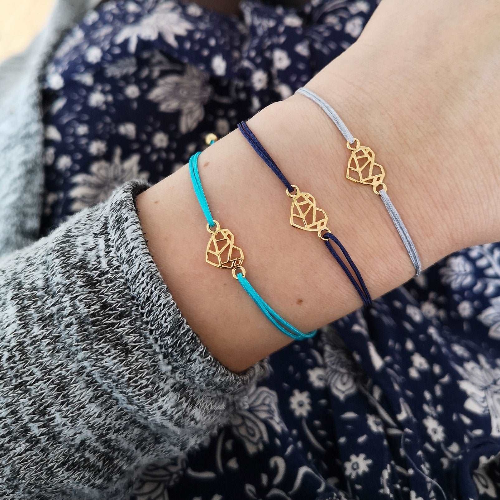 Tragefoto drei goldene Origami Herz Armbänder. Unteres Armband mit türkisem Band, mittleres Armband mit dunkelblauem Band und oberes Herz Armband mit grauem Band