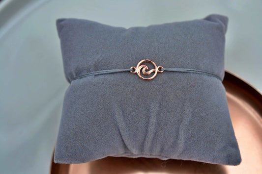 Roségoldenes Wellen-Armband mit grauem Band auf einem grauen Schmuckkissen