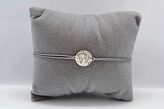 Weltkarte Armband silber mit grauem Band auf einem grauen Schmuckkissen
