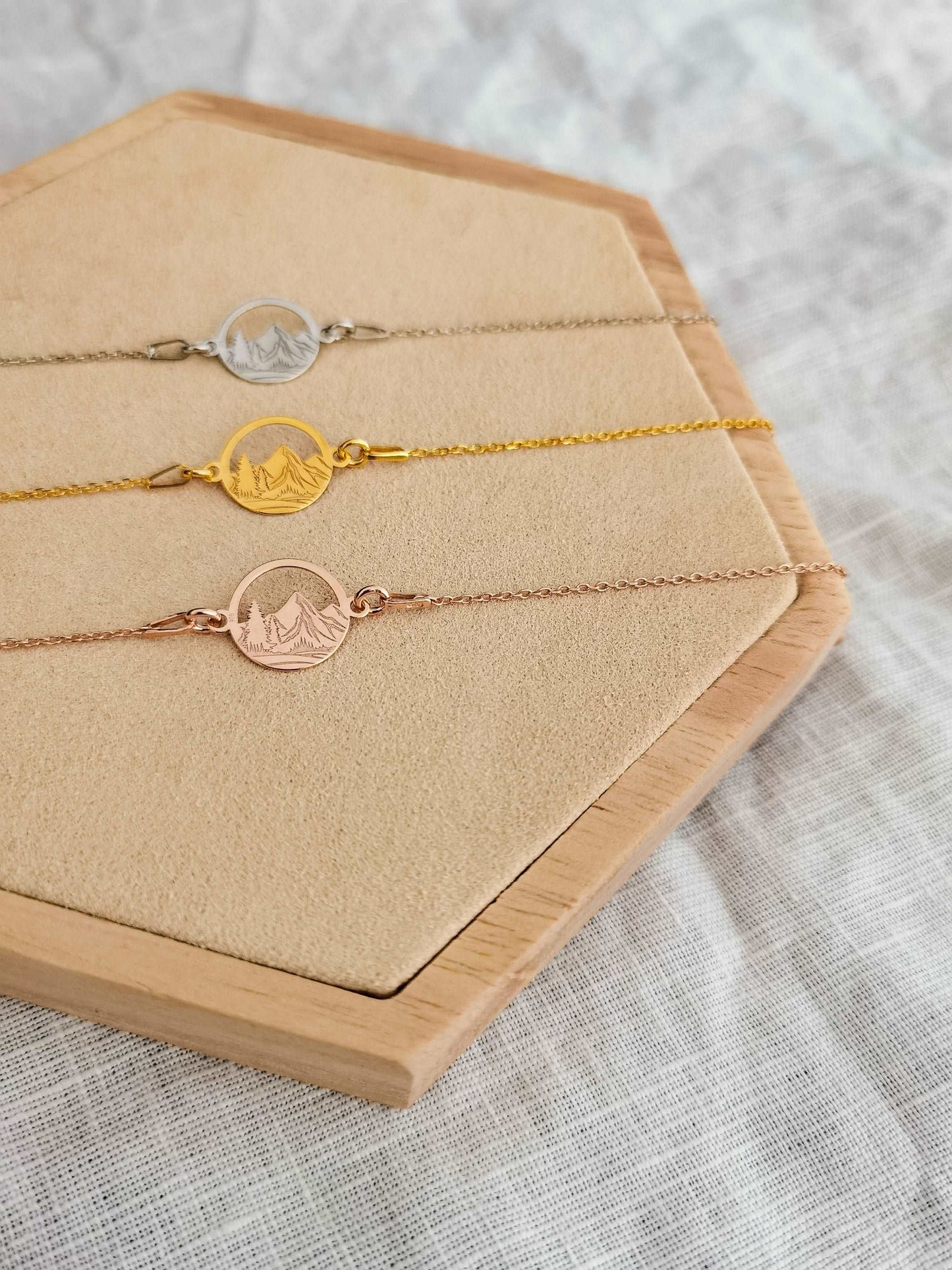 Drei Berg Armbänder in roségold, gold und silber liegen auf einem Holz Sechseck