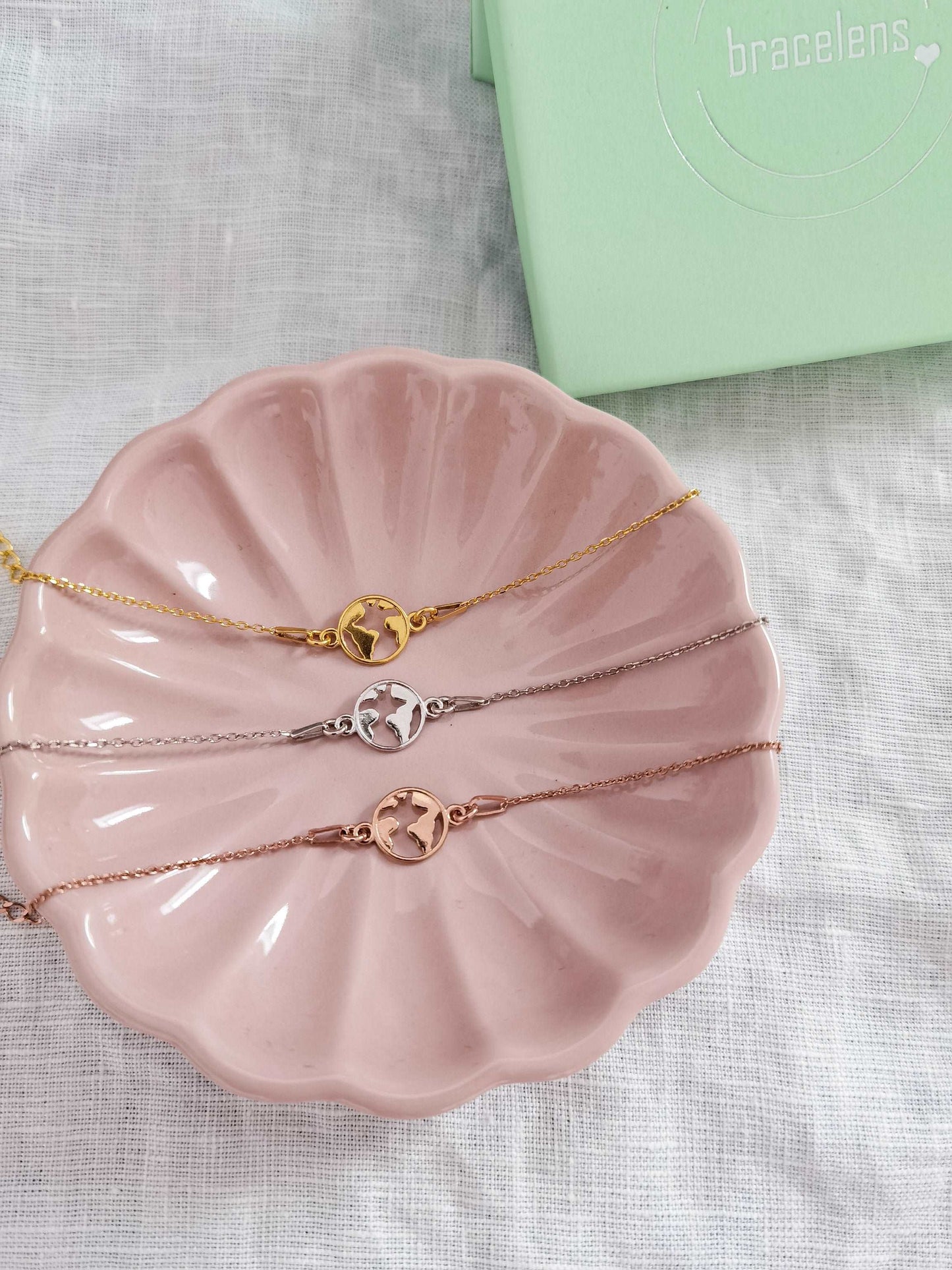 Weltkarte Armband in roségold, silber und gold in einer rosa Schmuckschale