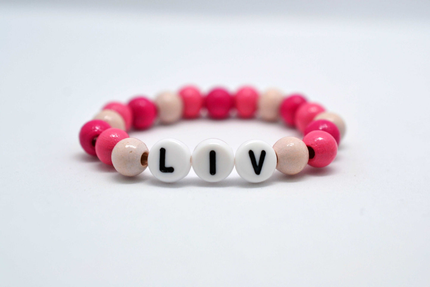 Personalisierbares Babyarmband mit Namen "Liv" und Holzperlen in rosa und pink