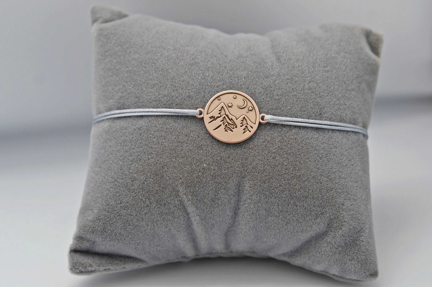 Roségoldenes Berg Armband mit grauem Band auf einem grauen Schmuckkissen