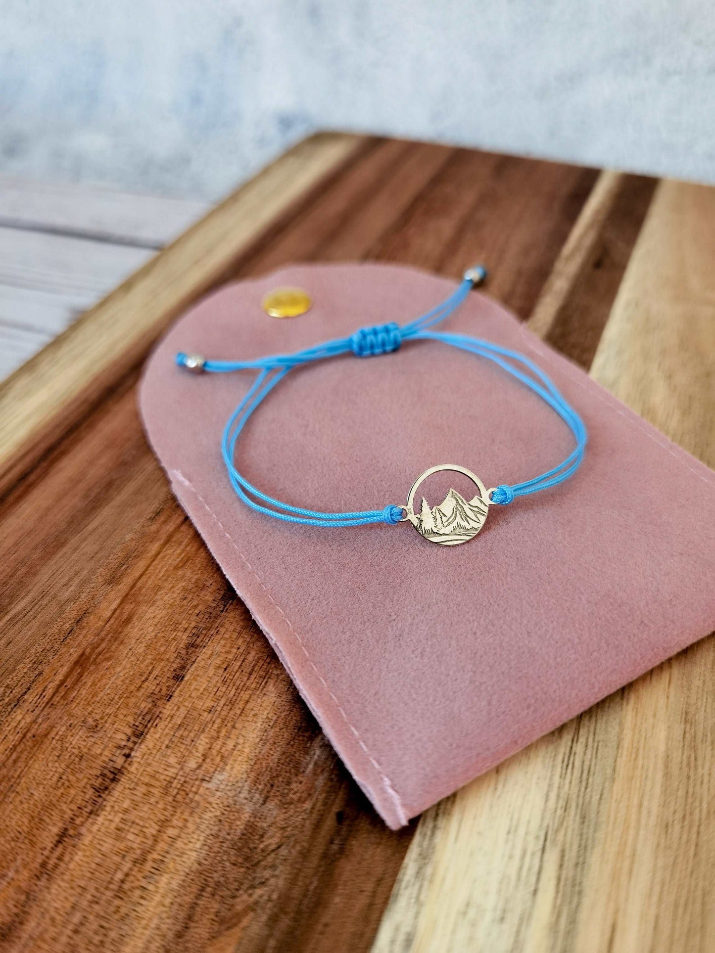 Ein silbernes Berg Armband mit babyblauem Band liegt auf einer rosa Schmucktasche auf einem dunklen Holztisch