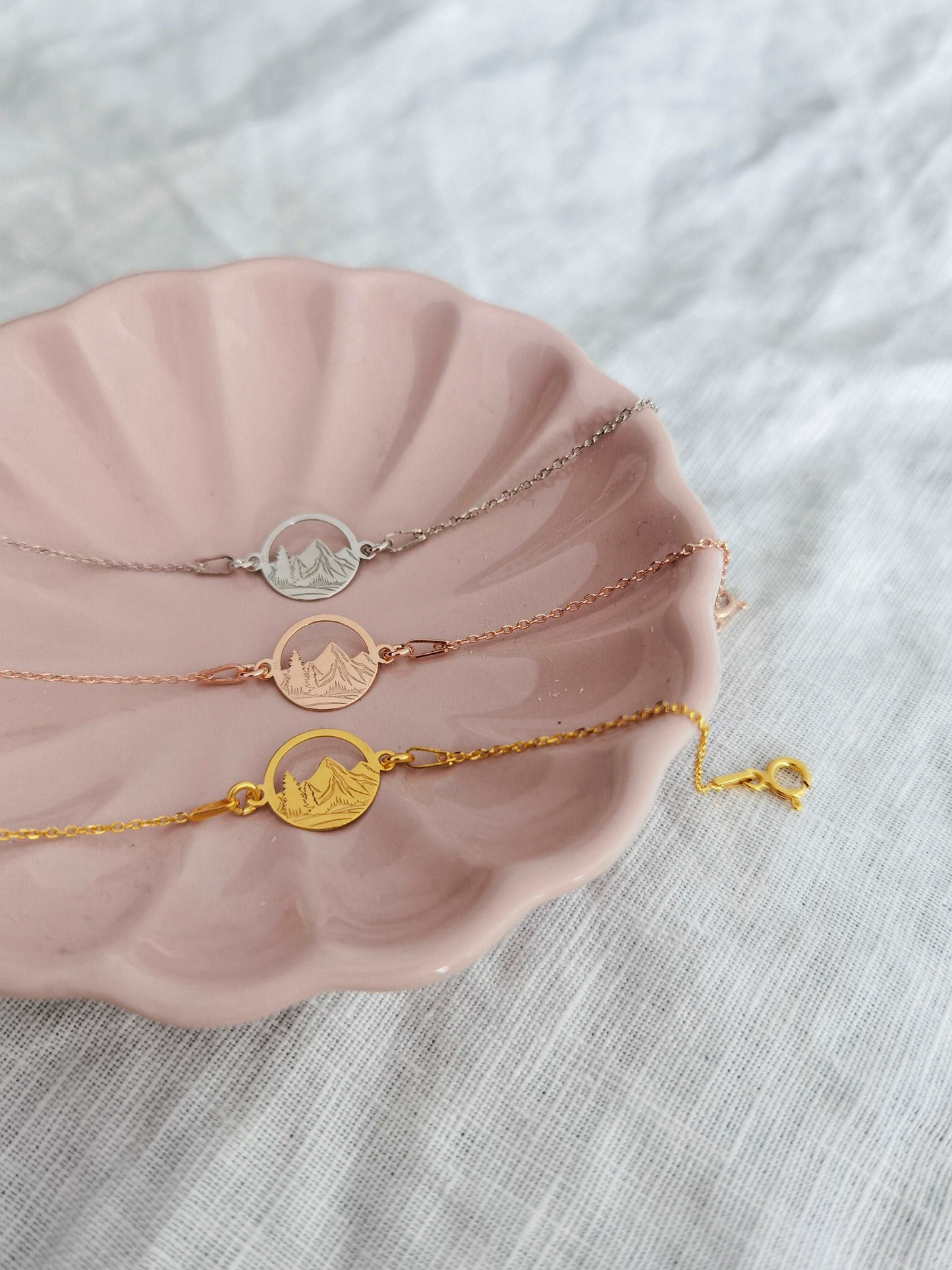 Drei Berg Armkettchen in gold, roségold und silber liegen in einer rosa Schmuckschale