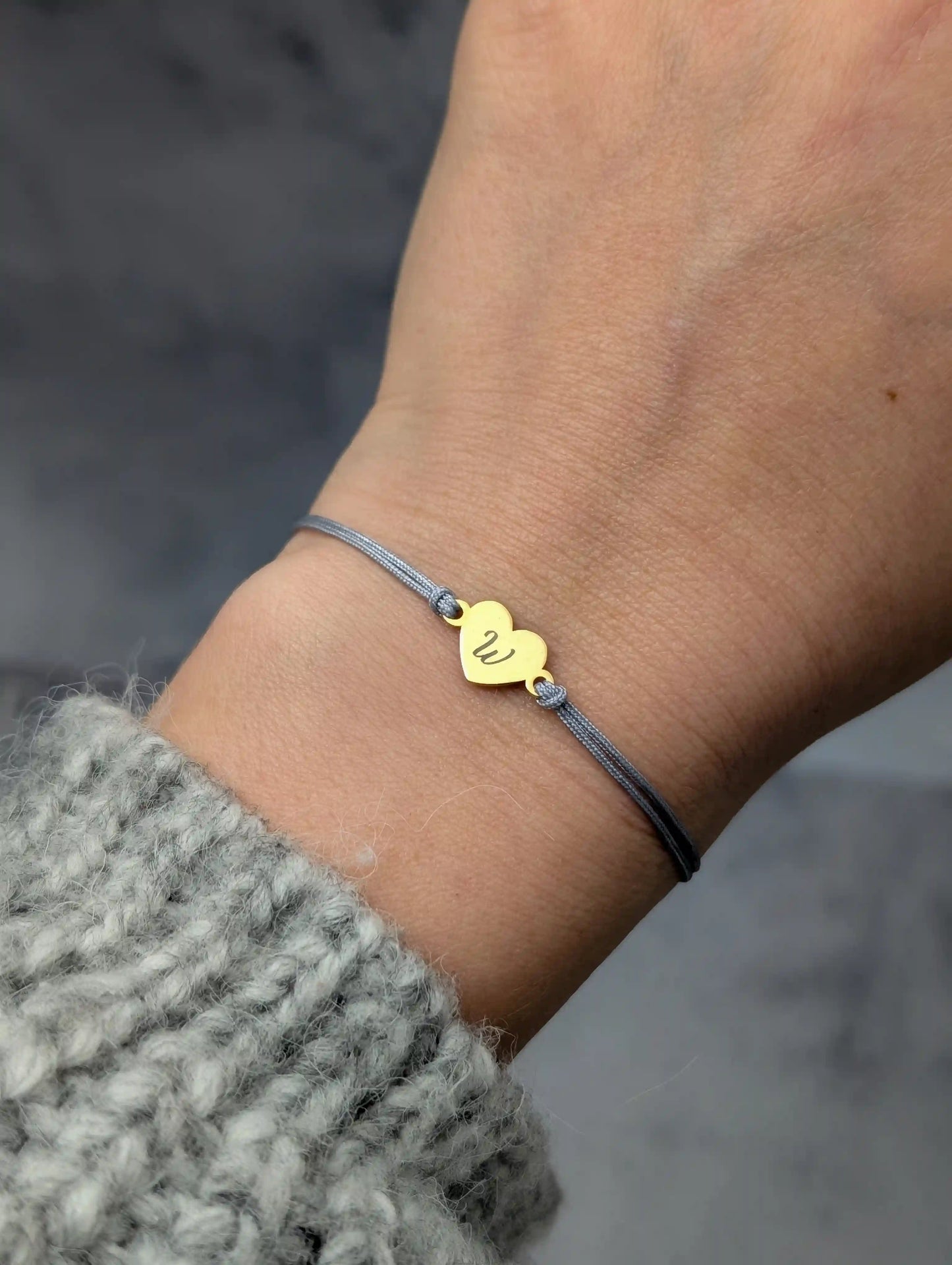 Tragefoto Gravur Armband. Graues Band, goldenes Herz mit dem Buchstaben "W"