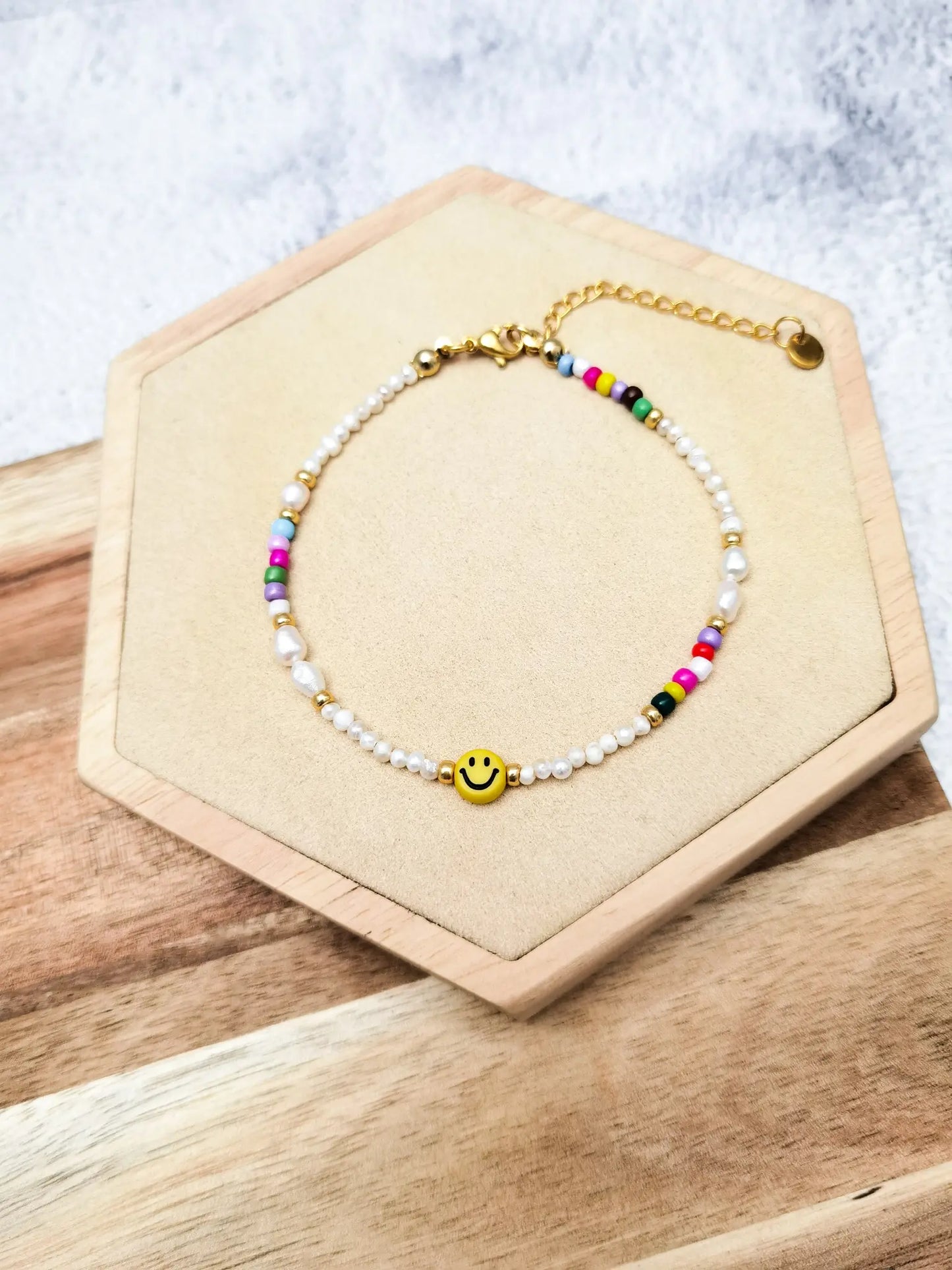Fußkette mit gelbem Smiley, kleinen Süßwasserperlen und kleinen bunten Perlen fotografiert auf einem Holz Sechseck