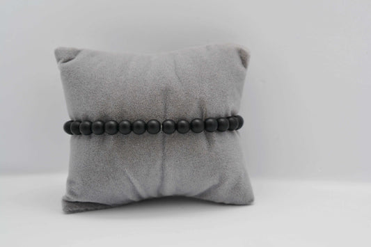 Armband aus matt schwarzen Jadeperlen auf einem grauen Schmuckkissen