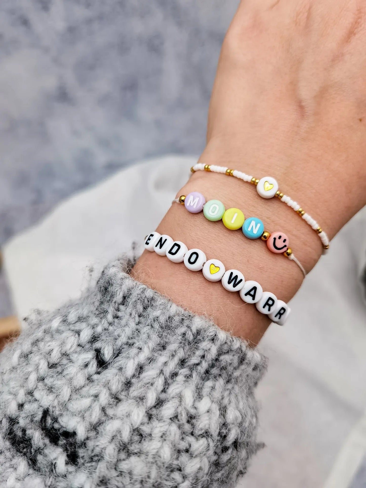 Tragefoto drei ArmbÀnder. 1x Endo Warrior Armband, 1x Armband "Moin" mit Smiley und 1x weià goldenes Armband mit Herzperle