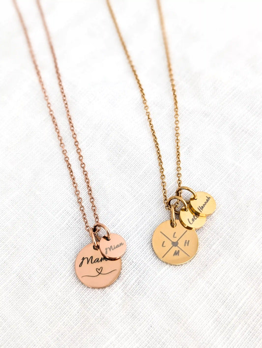 Roségoldene Kette mit Gravur "mama" auf dem großen Anhänger und Gravur "Mian" auf dem kleinen liegt neben einer Goldenen Kette mit "L, L, H, M" auf dem großen Anhänger und "Lotta" und "Hannah" auf zwei kleinen Anhängern