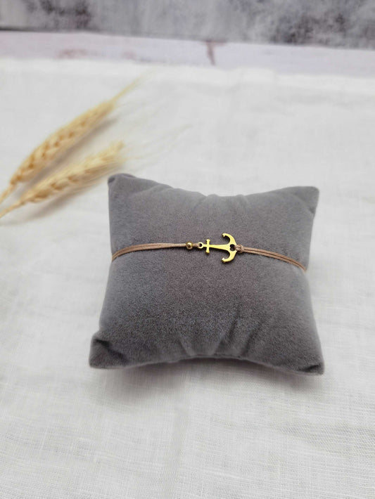 Anker Armband gold mit beigem Band aus Edelstahl auf einem Schmuckkissen