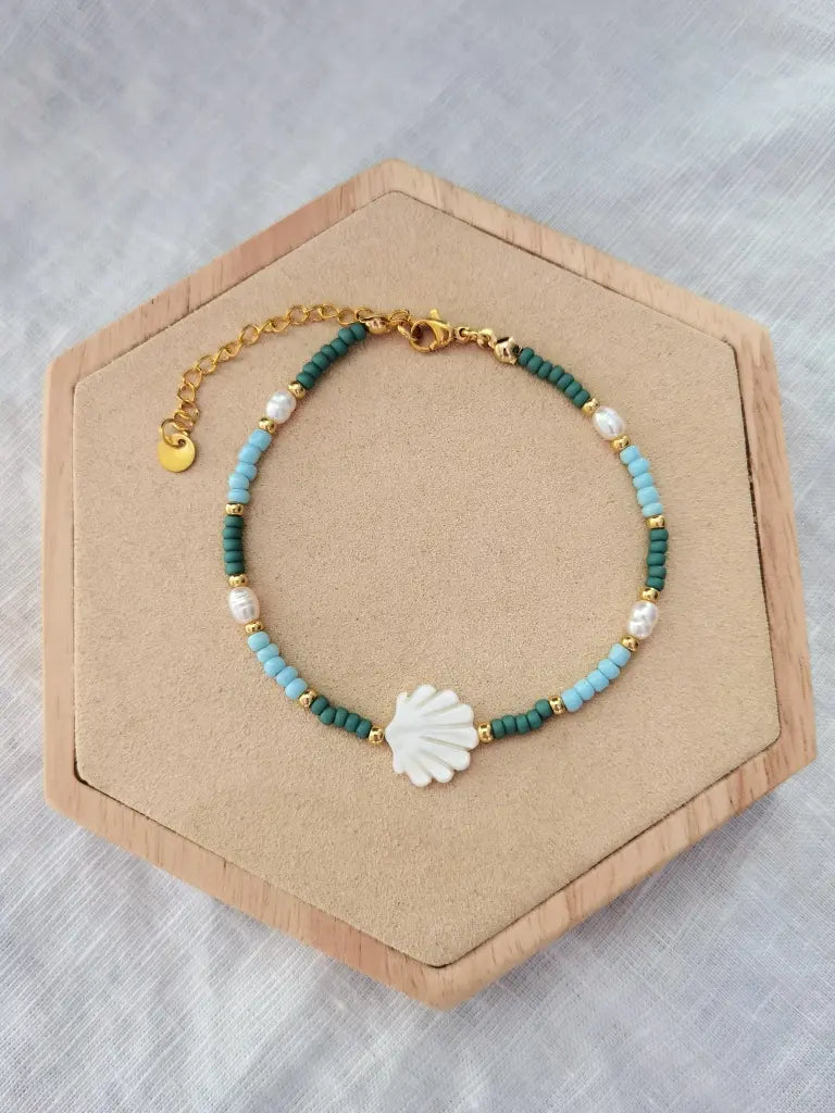 Muschel Fußkettchen mit einer weißen Jakobsmuschel, kleinen Glasperlen in grün, hellblau und gold und weißen Süßwasserperlen. Fußkette auf einem Holz Sechseck
