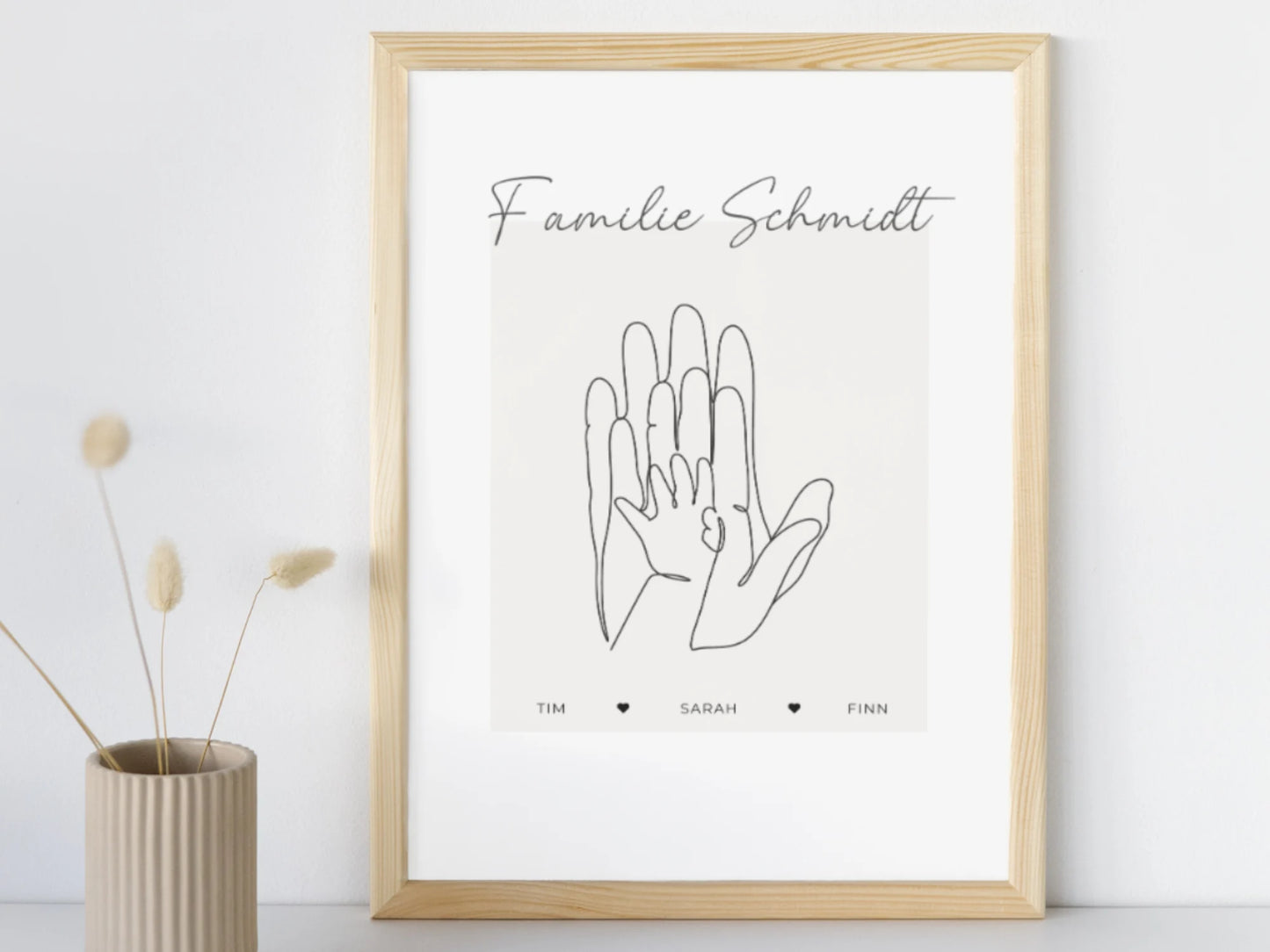Poster mit einem Familiennamen, drei Händen und darunter drei Vornamen mit Herzen dazwischen. Poster gerahmt in einem Holz Rahmen stehend an der Wand. Geschenkidee zur Geburt