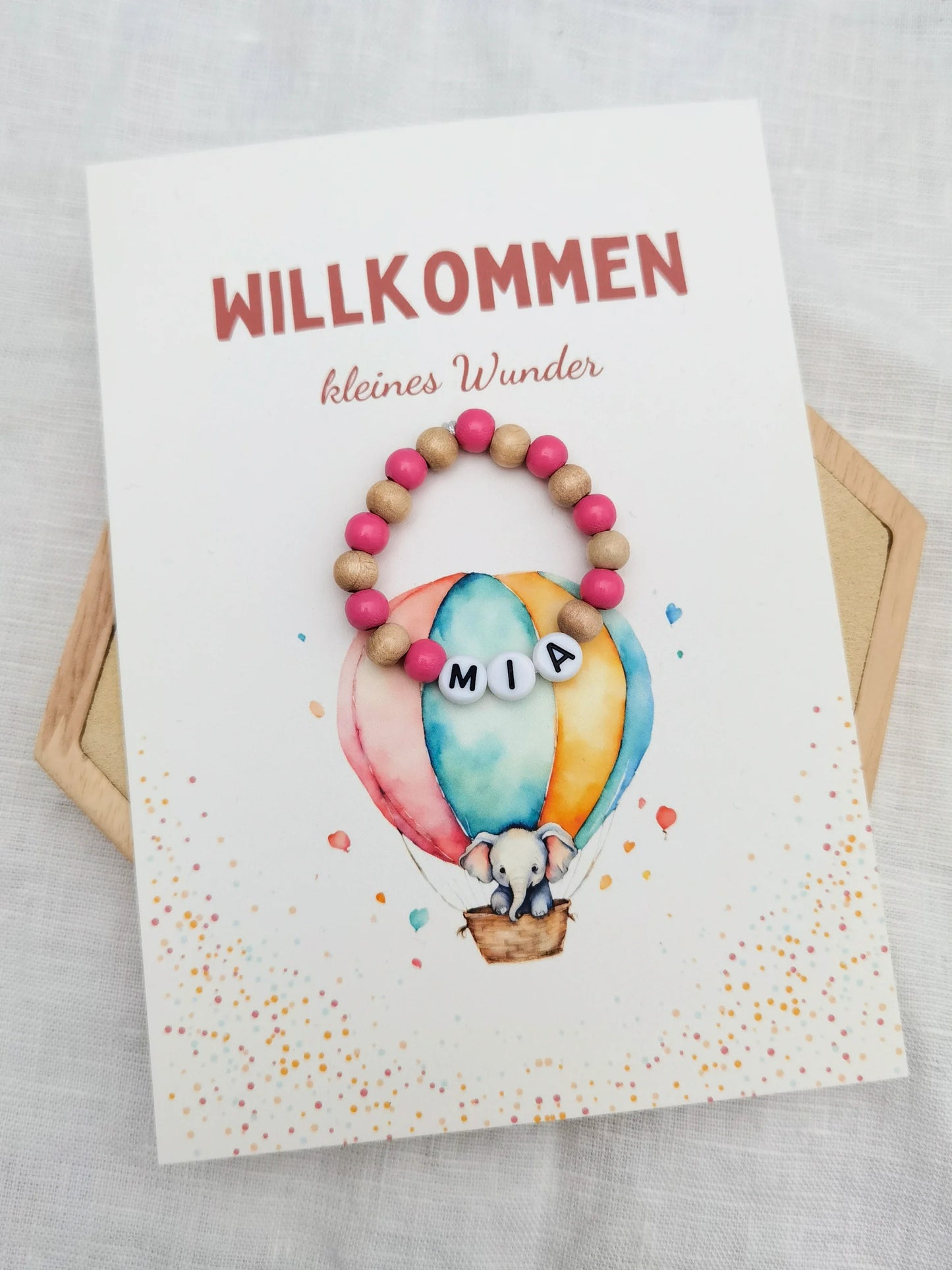 Postkarte mit Aufdruck "Willkommen kleines Wunder" und einem Babyarmband mit Wunschnamen