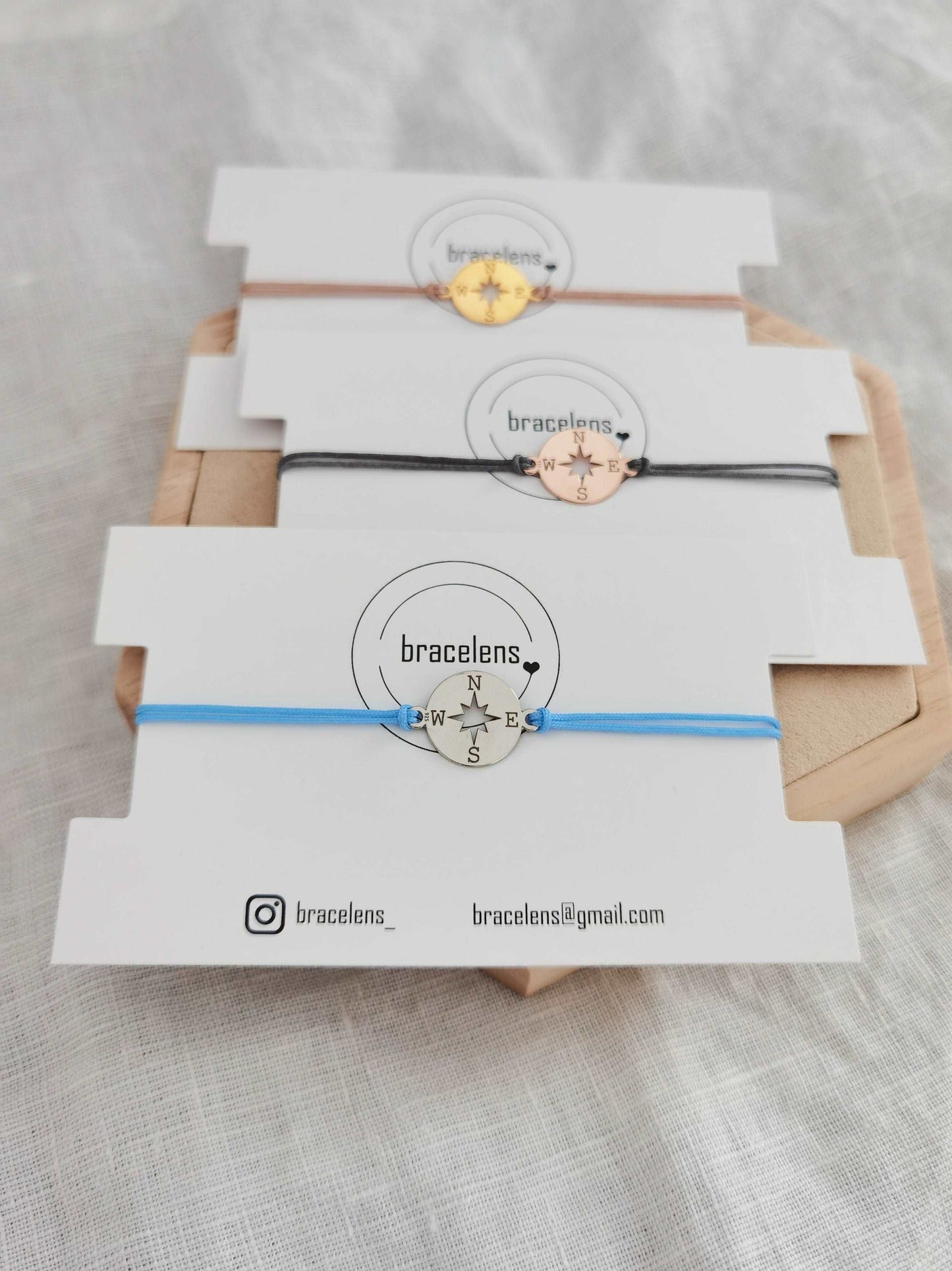 Kompass Armband silber mit hellblauem Band, roségold mit grauem Band und gold mit beigem Band jeweils auf einer weißen Schmuckkarte