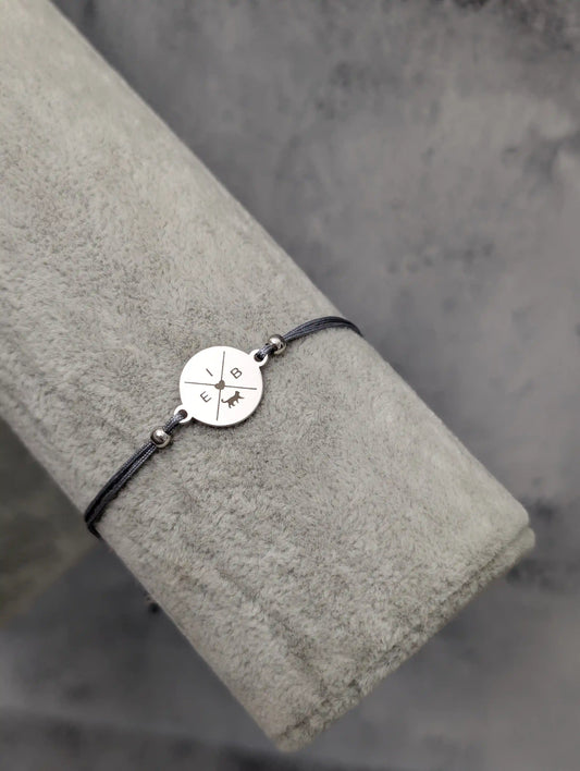 Ein graues Katzen Armband mit einem silbernen gravierten Plättchen mit Katzenmotiv und Buchstaben auf einem Schmuckständer aus grauem Samt fotografiert