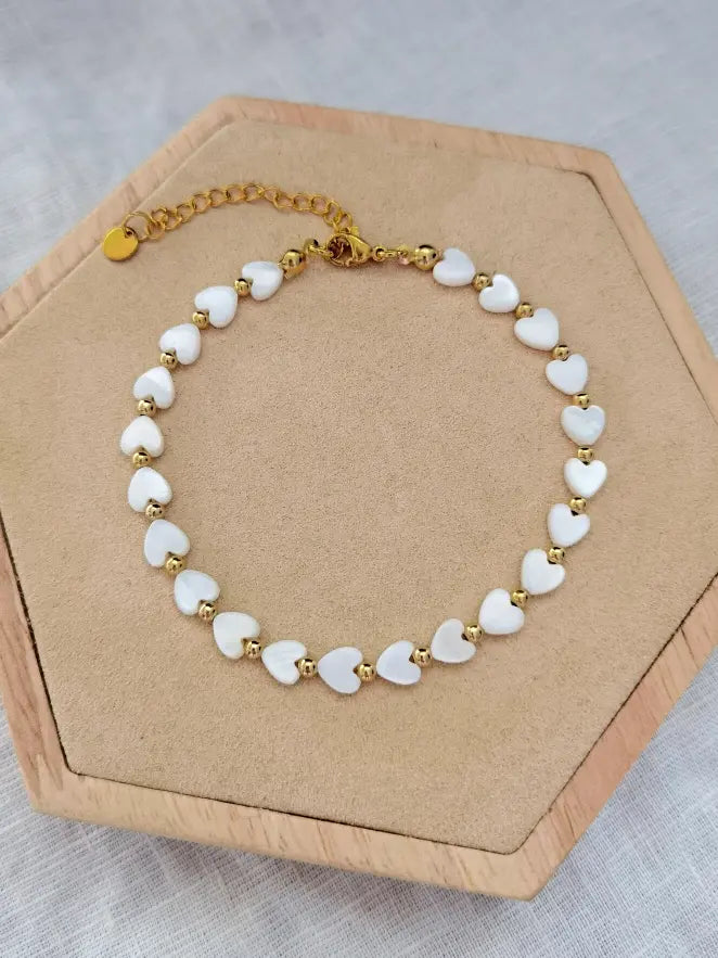 Fußkette mit weißen Perlmutt Herzen und kleinen goldenen Perlen dazwischen auf einem Holz Sechseck
