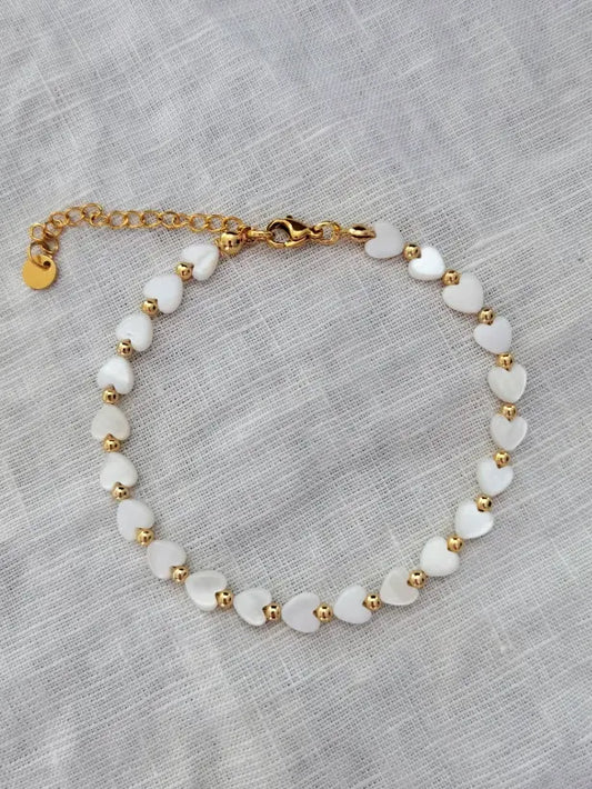 Fußkette mit weißen Perlmutt Herzen und kleinen goldenen Perlen dazwischen auf einem weißen Leinentuch