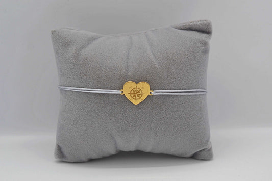 Herz Kompass Armband mit grauem Band und goldenem Herzen als Geschenk für Weltreisende. Fotografiert auf grauem Schmuckkissen