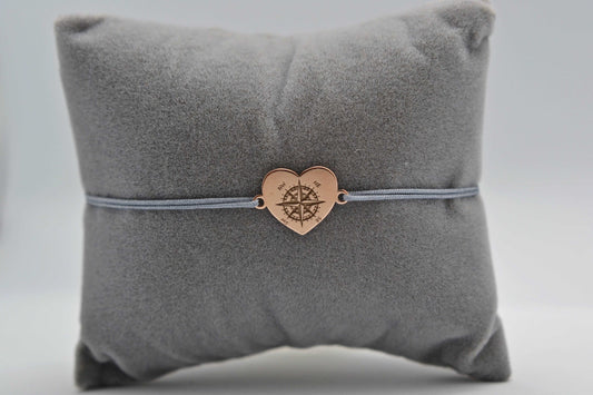 Herz Kompass Armband mit roségoldenem Herzen und grauem Band. Fotografiert auf einem grauen Schmuckkissen