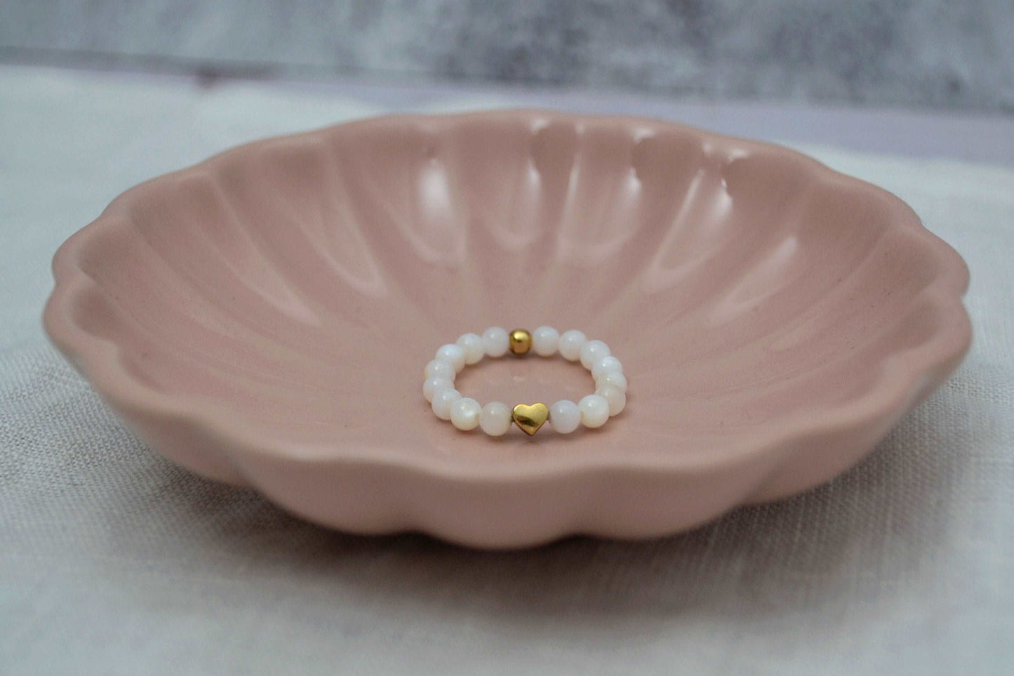 Weißer Perlenring mit roségoldenem Herz in rosa Schmuckschale