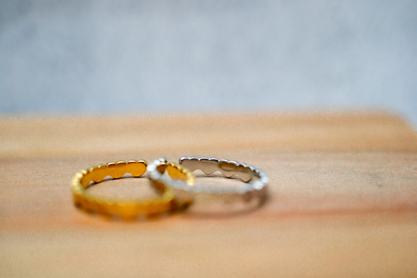 Ein goldener und ein silbener Herzchen Ring in Nahaufnahme auf einem Holzbrett fotografiert. Vorderer Bereich der Ringe unscharf dargestellt.
