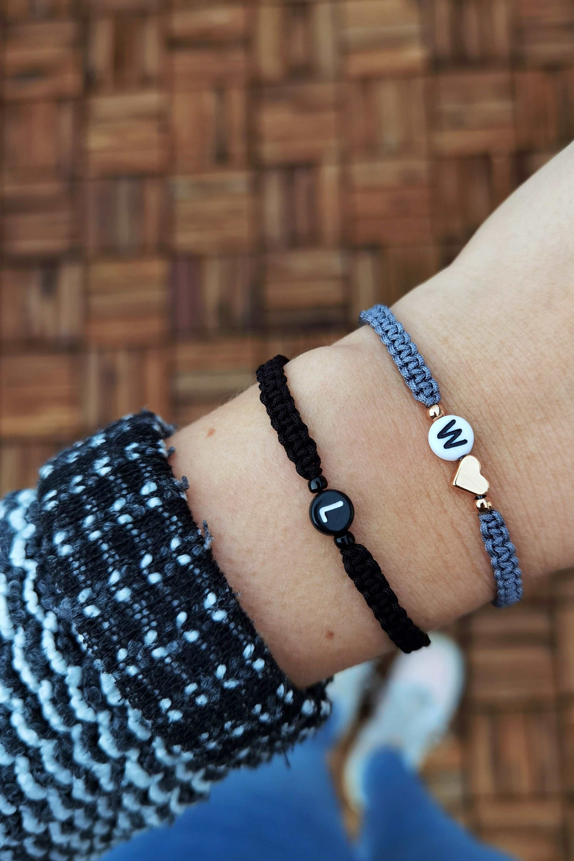 Tragefoto zwei Makramee Armbänder mit Buchstaben. Ein schwarzes Armband mit schwarzer Buchstabenperle "L" und ein graues Armband mit weißer Buchstabenperle "W" und roségoldenem Herz