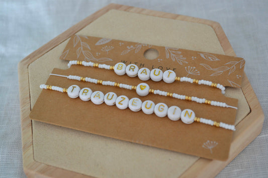 Drei gold weiße JGA Armbänder für Braut, Trauzeugin und die Crew auf einer braunen Schmuckkarte