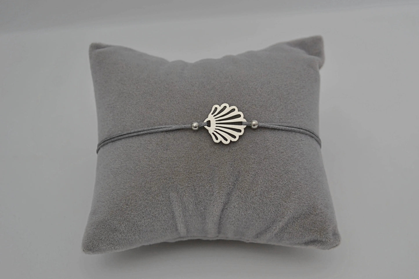 Jakobsmuschel Armband Edelstahl silber mit grauem Band auf einem grauen Schmuckkissen