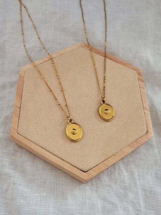 Zwei goldene Muschelkette aus Edelstahl auf einem Holz Sechseck. Eine Kette mit kleinen Kügelchen und eine Kette klassisch