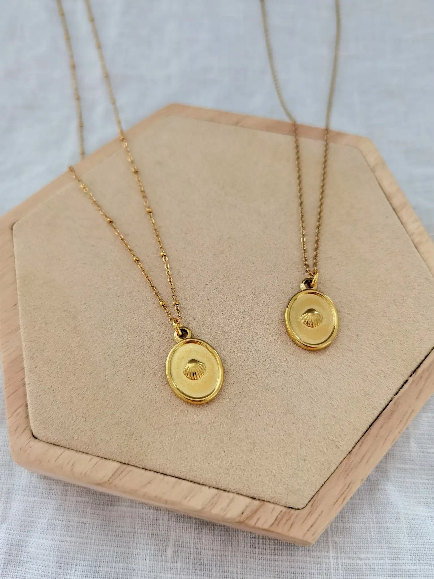 Zwei goldene Muschelkette aus Edelstahl auf einem Holz Sechseck. Jakobsmuschel Kette zum Beispiel als Jakobsweg Glücksbringer