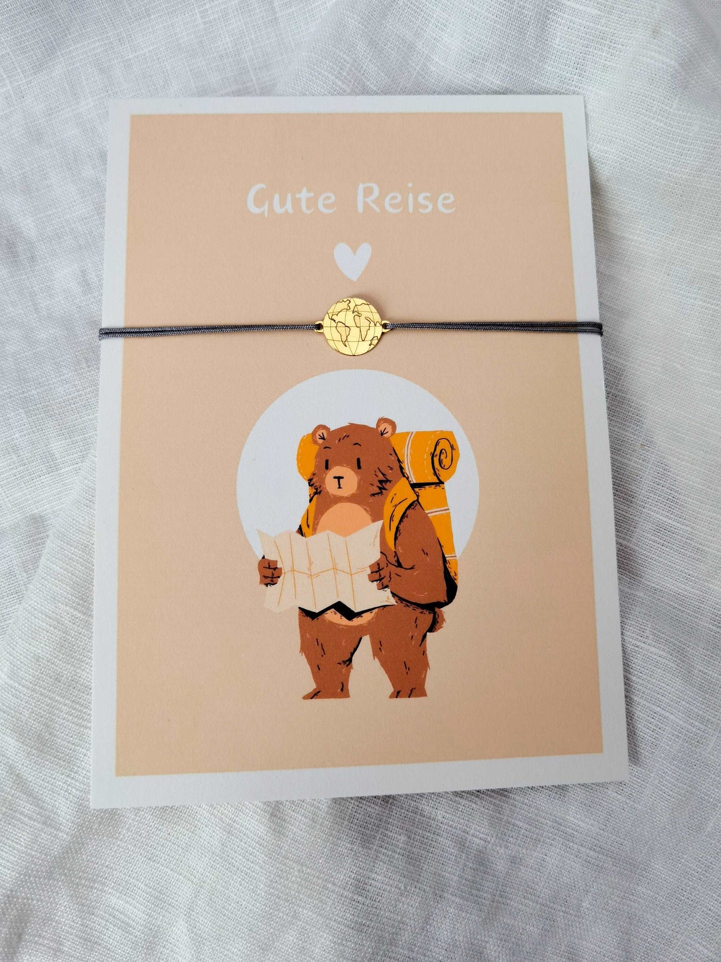 Karte Gute Reise mit Weltkarte Armband in gold und grau. Karte mit Aufdruck eines Bären, der einen Rucksack trägt und eine Landkarte in der Hand hält