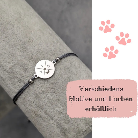 Silbernes Gravur Armband mit grauem Band. Auf dem silbernen Plättchen sin die Buchstaben E, I und B sowie eine Katze in einem Kreuz dargestellt