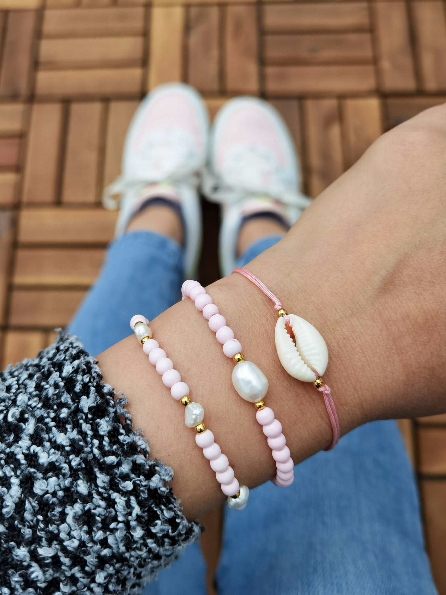 Tragefoto zwei Armbänder mit Süßwasserperlen und rosa Glasperlen, ein Kauri Muschel Armband mit goldenen Perlen und rosa Band