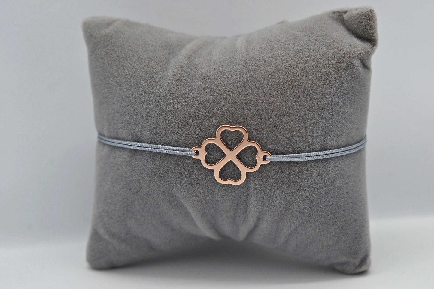 Kleeblatt Armband in roségold mit grauem Band auf grauem Schmuckkissen