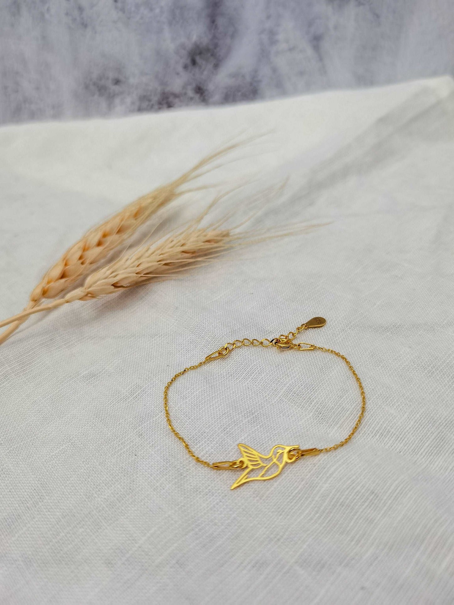 Goldenes Kolibri Armkettchen vor weiß grauem Hintergrund