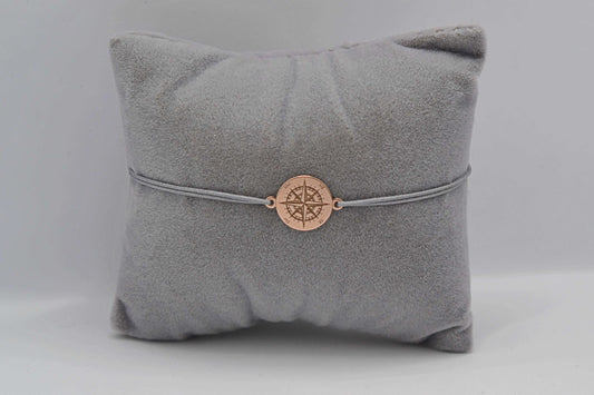 Roségoldenes Kompass Armband mit grauem Band auf einem grauen Schmuckkissen
