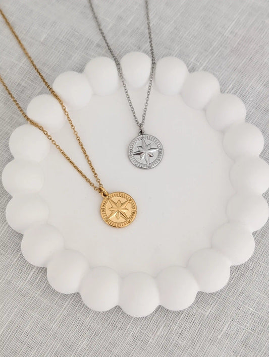 Kompass Kette in gold und silber auf einem weißen Untersetzer - Geschenk für Reisende